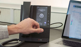 A man reaching for a landline on a desk beside a laptop.
