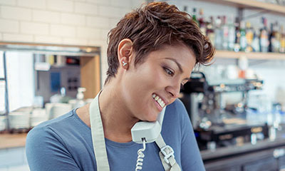 Woman with short brown hair on the phone in a apron and blue long sleeve