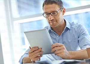 Man wearing glasses and blue button up looking at a tablet