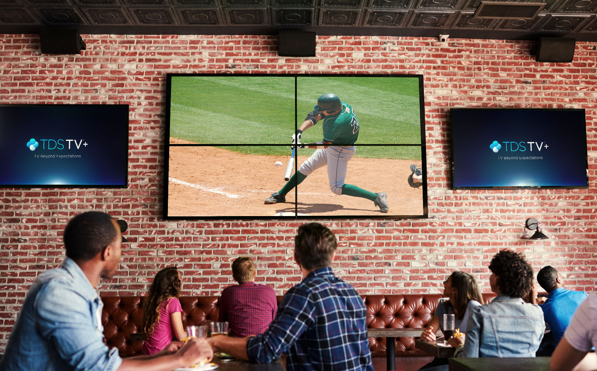 Group of people at a restaurant/bar watching baseball on a four panel TV