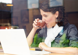 Woman drinking out of a brown cup and looking at a laptop
